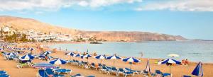 a beach with blue and white umbrellas and chairs at Casa Royal Los Cristianos Center in Los Cristianos