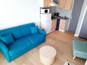 a living room with a blue couch and a kitchen at Studio piscine proche plage et village naturiste in Cap d'Agde +9 photos