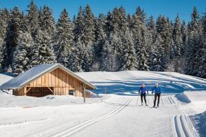 dos personas esquiando en la nieve frente a una cabaña en Studio 2 pers avec accès piscine et sauna, en Les Déserts
