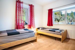 two beds in a room with red curtains and a window at Martina's Place in Castello di Fiemme
