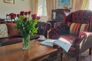 a living room with a table with a vase of flowers and a book at Graziers Cottage - character Cotswold cottage with inglenook, parking and pub nearby in Cheltenham