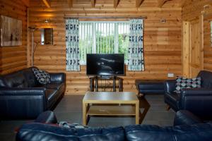 a living room with leather furniture and a flat screen tv at Teal Lodge - Nordic Log Cabin with private hot tub in Selby