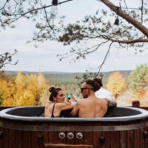 a man and a woman sitting in a hot tub at Jurty z widokiem, prywatna balia- DZIKOLAS GLAMPING in Krasnobród