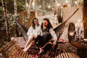 a man and a woman sitting on a hammock at Jurty z widokiem, prywatna balia- DZIKOLAS GLAMPING in Krasnobród