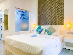 a white bedroom with a large white bed with blue pillows at Velana Beach Hotel Maldives in Maafushi