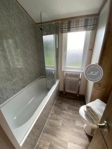 La salle de bains est pourvue d'une baignoire, de toilettes et d'une douche. dans l'établissement The Retreat Hot Tub Lodge - Golden Palm Resort (21), à Skegness