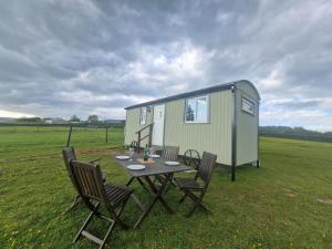 a table and chairs and a tiny house in a field at Cwtch Glamping Shepherds Huts in Abergavenny