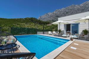 a swimming pool with chairs and a house with a mountain at Family & Child friendly Villa Violet with Salt water pool in Makarska