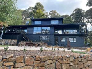 a large black house with a stone wall at Sweeping views of Hanging Rock and Cobaw Ranges in Mount Macedon
