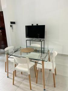 mesa de cristal con sillas blancas y TV de pantalla plana. en sandi house en San Salvador de Jujuy
