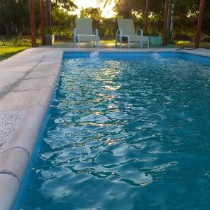 una piscina con 2 sillas blancas. en Finca Los Chichelos en Santiago del Estero