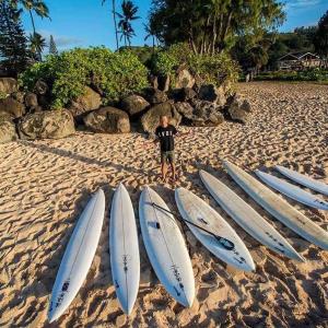 a man standing next to four surfboards on a beach at Haryugetu Guesthouse in NASA in Kaiyo