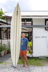 a man holding a surfboard in front of a building at Haryugetu Guesthouse in NASA in Kaiyo