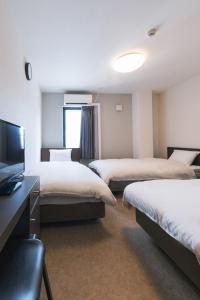 大阪市にあるOKINI HOTEL nambaのベッド3台、薄型テレビが備わるホテルルームです。