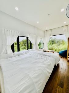 Măng Đen Land - Homestay&Coffee في Kon Von Kla: سرير أبيض كبير في غرفة بها نوافذ