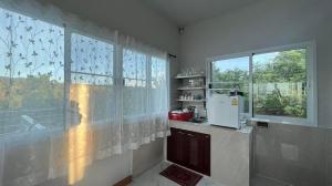 eine Küche mit einem Fenster mit Vorhängen und einem Kühlschrank in der Unterkunft Family Hill Khaokho บ้านพัก กางเต็นท์ วิวภูเขา in Khao Kho