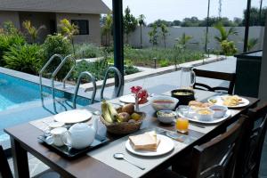 a table with breakfast food on it next to a pool at SaffronStays Eden, Nashik - pet-friendly villa with pool, jacuzzi & grape farm in Nashik
