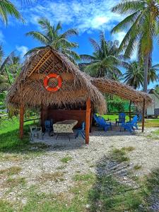 a straw hut with a table and chairs and palm trees at Moanarani Camping in Avatoru