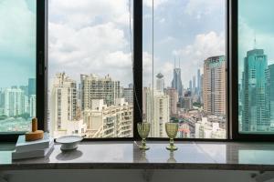uma vista para o horizonte da cidade a partir de uma janela com 2 copos de vinho em Shanghai Yi DU Apartments Downtown - near Nanjing West Road subway em Xangai