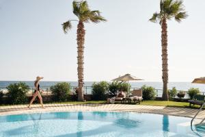a woman walking by a swimming pool with palm trees at Ikaros Beach, Luxury Resort & Spa - Adults Only in Malia