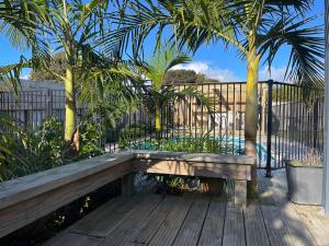 a wooden bench sitting on a deck with palm trees at Surf Stay Ahipara - 200m to the beach 2m to the pool in Ahipara