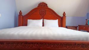 a large bed with a wooden headboard and white sheets at I AM Koh Ker in Phumĭ Mréch