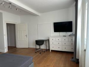 a white bedroom with a television on a dresser with a chair at Charmante Altbauwohnung in Erlangen