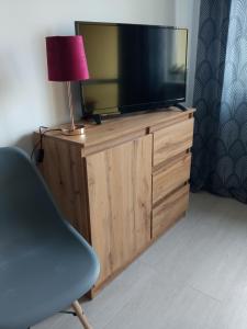 a television on a wooden dresser with a lamp and a chair at Słoneczne Centrum Apartament in Suwałki