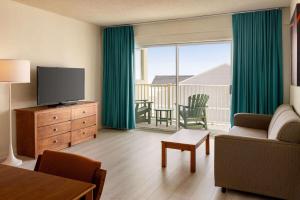 a living room with a couch and a television and a balcony at Howard Johnson by Wyndham Ocean City Oceanfront in Ocean City