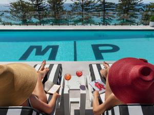 Dos personas sentadas en sillas junto a una piscina en Manly Pacific Sydney MGallery Collection en Sídney