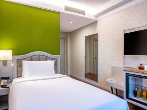 - une chambre avec un lit blanc et un mur vert dans l'établissement Mercure Tbilisi Old Town, à Tbilissi