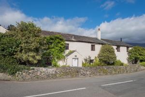 a white house with a stone wall next to a street at farmhouse braithwaite mews in Keswick