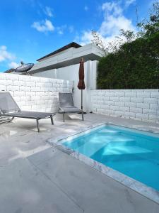 a swimming pool with two chairs and an umbrella next to a wall at Ida Japanese pool villa in Chalong 