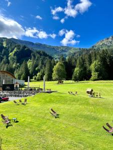 a grassy field with chairs and a building and mountains at Hameau des Prodains - Hôtel in Morzine