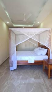 a bed with a canopy in a room with a table at Linda's Little Lincoln in Watamu