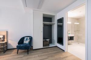 Habitación con silla azul y baño. en YParc Hôtel, en Yverdon-les-Bains