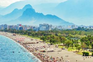 ein Strand mit Sonnenschirmen und Menschen darauf mit Bergen im Hintergrund in der Unterkunft DIAMOND luxury Hotel in Antalya
