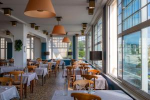 VTF L'Hotel Des Bains في سانت كاست-لو-غيلدو: مطعم بطاولات وكراسي ونوافذ كبيرة