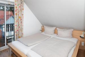 uma cama com lençóis brancos num quarto com uma janela em Dallacker 8, FeWo 3 em Duhnen