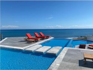 a swimming pool with red lounge chairs and the ocean at Villa E11even con C hef Privado Ocean Front in Isla Mujeres