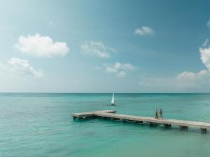 two people walking on a dock in the water with a sailboat at Hyatt Zilara Cap Cana - Adults Only in Punta Cana