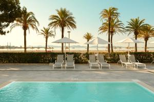 a pool with white chairs and umbrellas and palm trees at Sunwing Alcudia Beach in Alcudia