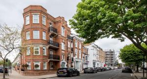 un bâtiment en briques rouges avec des voitures garées devant lui dans l'établissement Kensington Olympia Apartment, Breakfast, à Londres