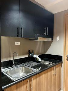 a kitchen with a sink and black cabinets at Pasay Condotel with Massage Chair and PS4- Stellar Suites in Manila