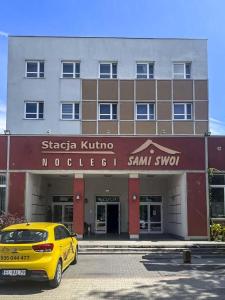 een gele auto geparkeerd voor een gebouw bij Sami Swoi Kutno in Kutno