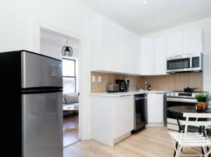 a kitchen with white cabinets and a black refrigerator at Stunning 3BR Apartment in NYC! in New York