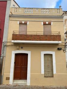 Edificio amarillo con balcón y 2 puertas en Alojamiento Orellana, en Orellana la Vieja