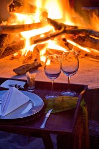 two wine glasses sitting on a table in front of a fire at Duma Manzi Eco Lodge & Spa in Richmond