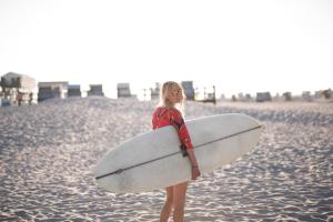 a woman standing on the beach holding a surfboard at Beach Motel St. Peter-Ording in Böhl