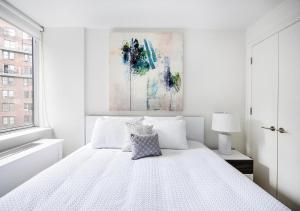 Stunning 2 BED 2 BA At UES في نيويورك: غرفة نوم بيضاء بسرير ابيض ولوحة
